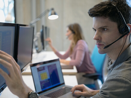 2 people sitting at computers, talking via headsets.